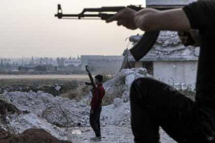 A pro-Turkish Syrian fighter holds an assault rifle at a camp for people displaced by conf