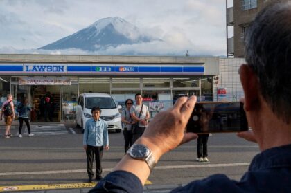 Tourists take pictures of Mount Fuji from opposite a convenience store in the town of Fuji