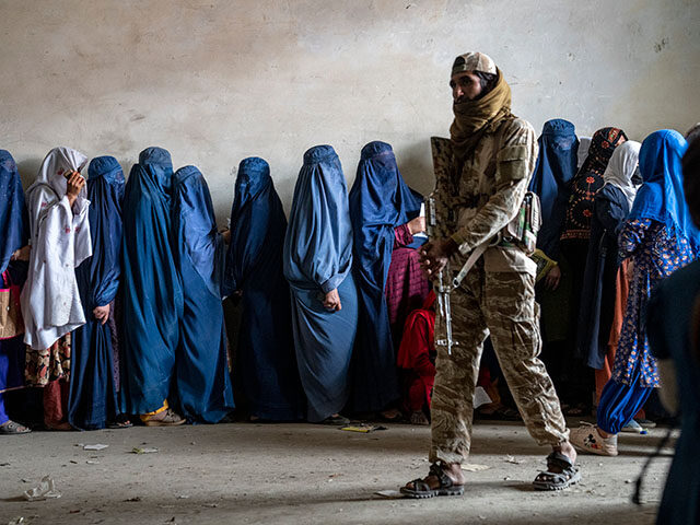 A Taliban fighter stands guard as women wait to receive food rations distributed by a huma