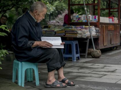 An elderly man reads a book beside a bookstall in a park. Chinese government tries to prom