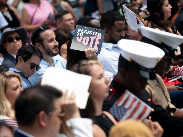 A person holds a sign reading "Register to Vote" during a naturalization ceremon