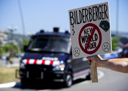 A placard against the Bilderberg Group meeting is held in front of a anti-riot van on June