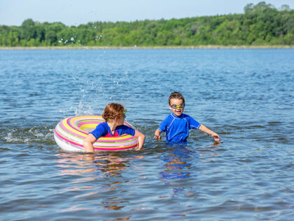 Girl and her younger brother swimming and playing in the lake on a beautiful summer day. T