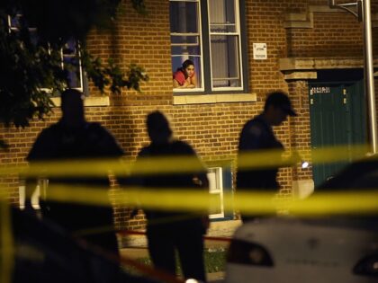 CHICAGO, IL - JULY 19: A woman watches from her window as police look for evidence after 2