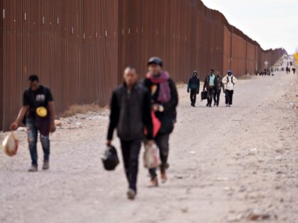 Migrants walk along the US-Mexico border border fence in Lukeville, Arizona, US, on Monday