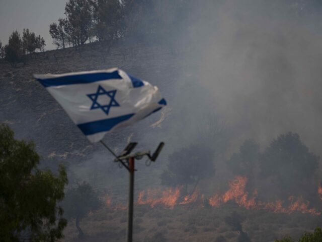 An Israeli flag flutters next to a fire burning in an area near the border with Lebanon, n