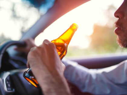 Drunk asian young man drives a car with a bottle of beer - stock photo