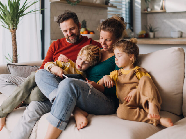 Little children bonding with parents on sofa at home and using tablet. - stock photo