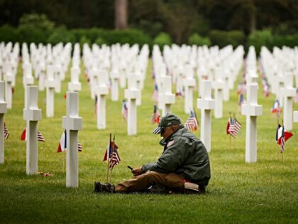 FILE - A man sits by gravestones in the the American Cemetery during a ceremony to mark th
