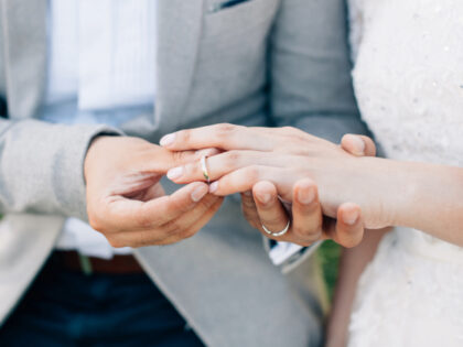 Groom putting ring on bride's finger. Rings exchange. Happy couple celebrating wedding out