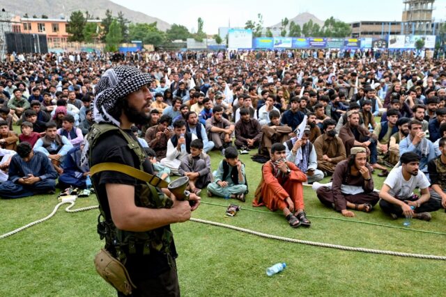 Afghan security personnel keeps guard as fans watch a live broadcast of the game