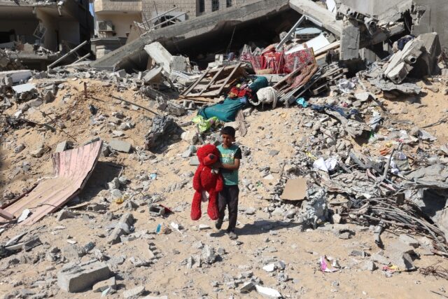 A Palestinian child walks with a toy bear recovered from the rubble of a destroyed buildin