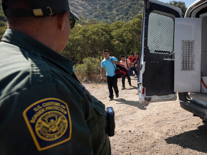 A Border Patrol agent leads a group of migrants seeking asylum towards a van to be transpo