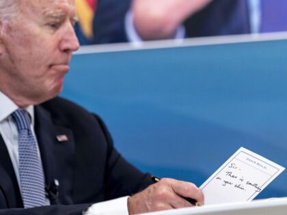 President Joe Biden holds a card handed to him by an aide that reads "Sir, there is s