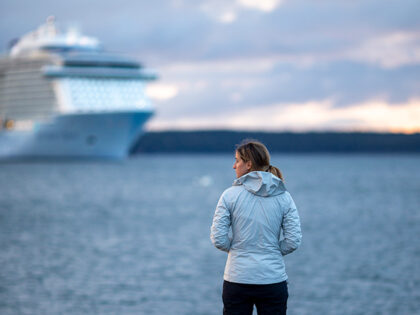 Woman stands on dock with massive cruise ship in distance - stock photo