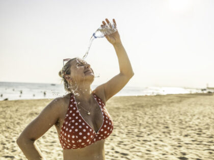 A young woman on the beach cools down with cold water during the summer heat.