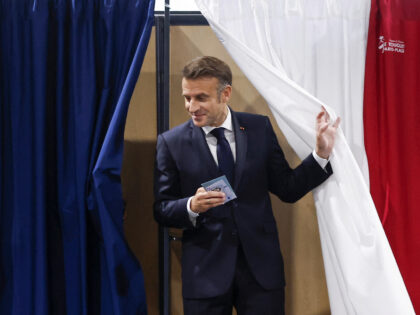 TOPSHOT - France's President Emmanuel Macron exits a polling booth, adorned with curtains