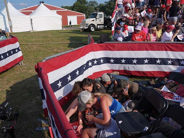 Members of the crowd duck under chairs after former president Donald Trump is assisted off