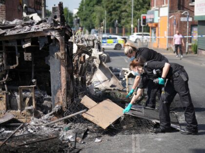 LEEDS, ENGLAND - JULY 19: Forensic scientists examine a burnt out bus, as police patrol th