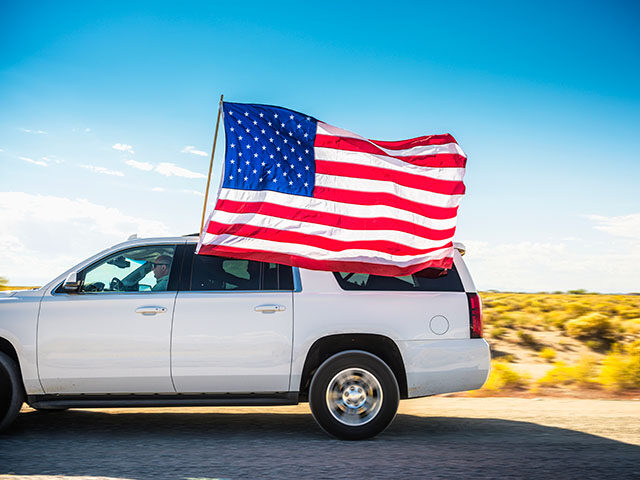White SUV driving with passenger holding American flag
