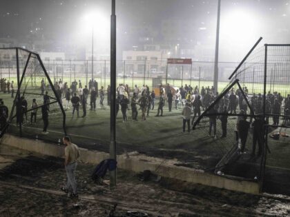 Residents and authorities stand at a soccer field that was hit by a rocket, killing multip