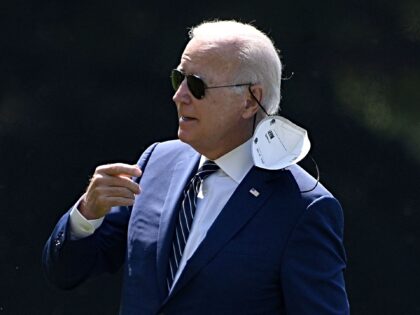 US President Joe Biden removes his face mask as he walks on the South Lawn of the White Ho