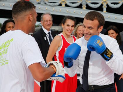 French President Emmanuel Macron (R) spars with a boxing partner on a barge floating on th