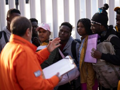A Mexican immigration official speaks to migrants, including many Haitians, as they line u