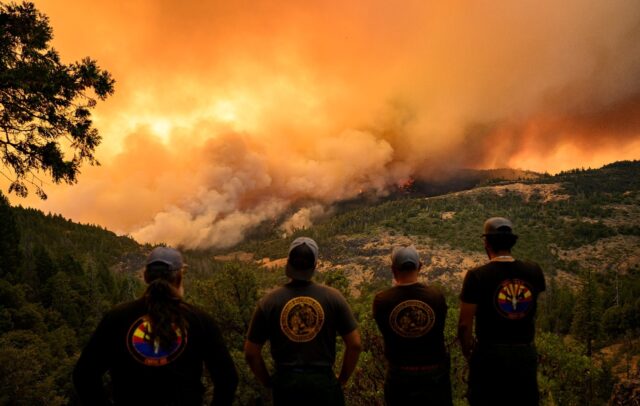 Firefighters watch as flames and smoke move through a valley in the Forest Ranch area of B