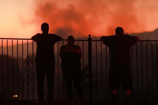 People watch as a wildfire burns close to properties in Riverside, California, on July 21,