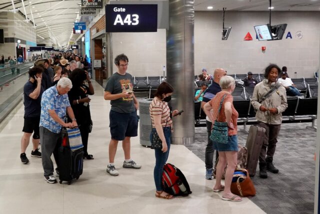 Travelers wait in a long line to speak with a Delta representative at the help desk in the