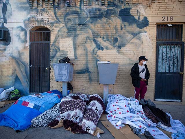 Covered with blankets, migrants sleep on a street in downtown El Paso, Texas, Sunday, Apri