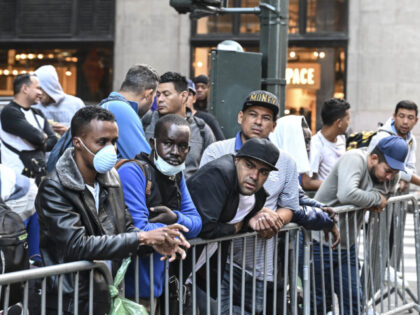 Migrants line up outside Roosevelt Hotel while waiting for placement inside a shelter as a