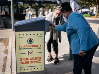 An election observer assists a voter as she drops off an absentee ballot into a drop box o