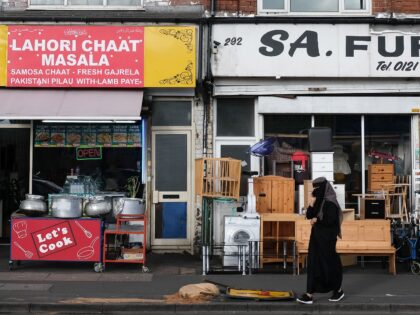 A woman passes a row of shops in the Sparkbrook area of Birmingham, central England, Augus