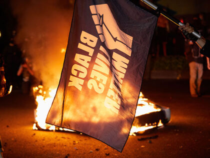 A Black Lives Matter flag waves in front of a fire at the North Precinct Police building i