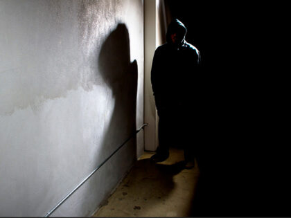 Photo of a hooded criminal stalking in the shadows of a dark street alley.