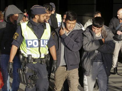 A group of migrants off an incoming train walk down a platform as they are accompanied by