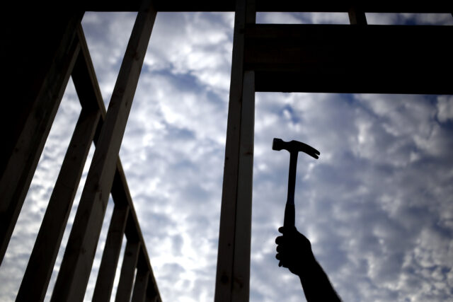 The silhouette of a contractor is seen hammering wood framing for a house under constructi