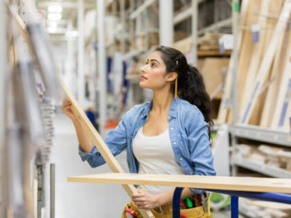 Confident young Middle Eastern female home improvement store employee loads wooden planks