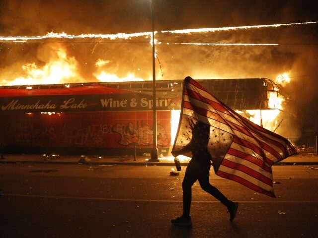 A protester carries a U.S. flag upside down, a sign of distress, next to a burning buildin