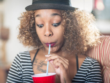 A woman drinks from a straw while making a funny face.