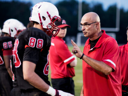 A football coach explains things to his player on the field.