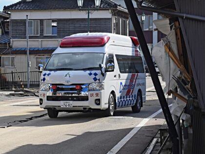 An ambulance manoeuvrers around cracks in the road while passing by a tilted house and roa