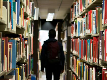 man with backpack beside a books