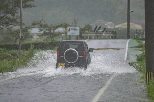 A car drives through a flooded street in Yufu city of Oita prefecture