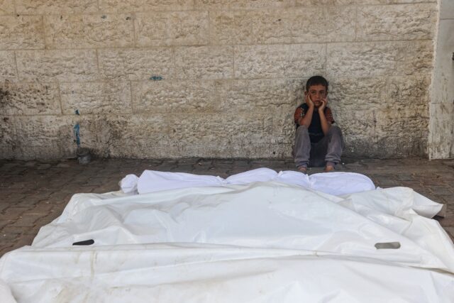 A child sits beside the shrouded corpses of people killed in an overnight Israeli strike,