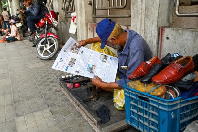 A cobbler reads a newspaper along a street in Dhaka days after prime minister Sheikh Hasin