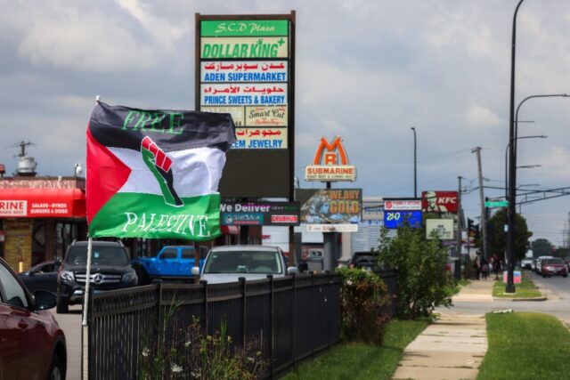 Palestinian flags flutter in the wind, shops display signs in both Arabic and English, and