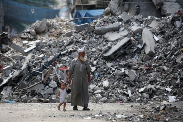 Palestinians walk past ruins in Al-Bureij refugee camp in central Gaza, more than 10 month